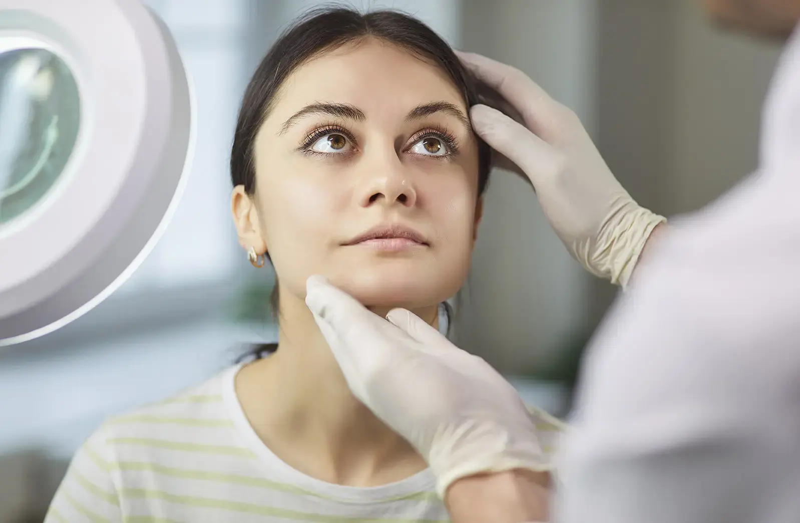 An eyelid enhancement surgeon assessing a female patient's facial anatomy during consultation.