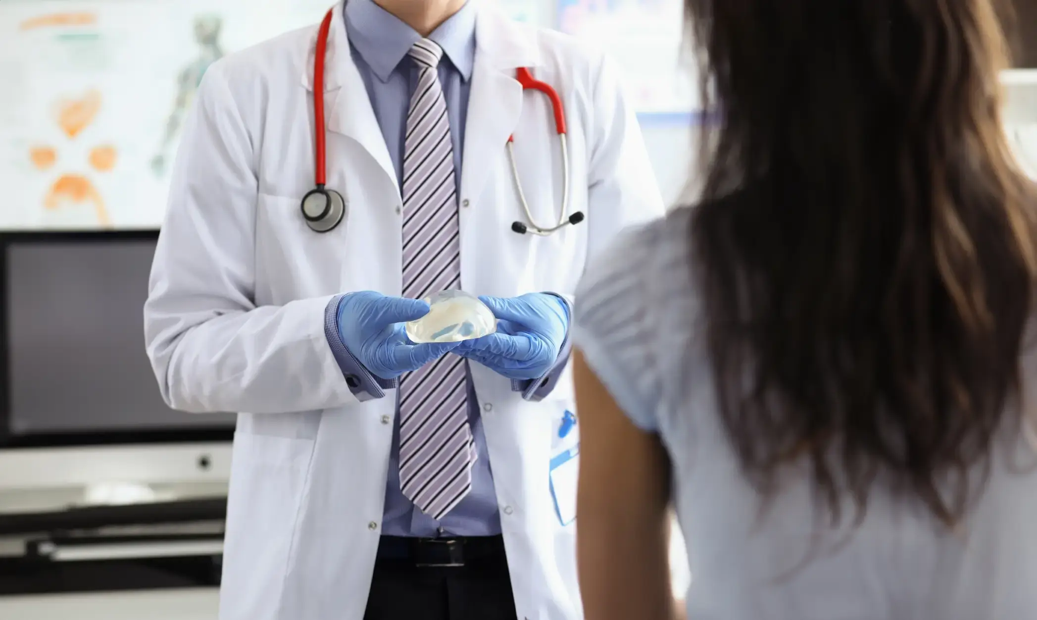 Plastic surgeon discussing breast enlargement options while showing a breast implant during a preoperative patient consultation